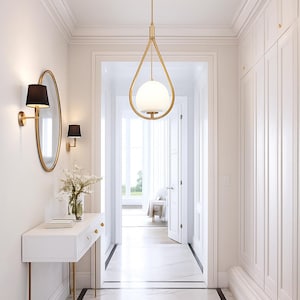 May include: A bright hallway with white walls, a marble floor, and gold accents. A gold pendant light with a spherical white shade hangs in the center. A white console table with gold legs and a gold-framed mirror are on the left.