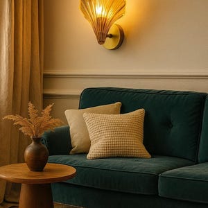 Puede incluir: Una lámpara de pared de vidrio ámbar y base dorada ilumina una sala de estar. Un sofá verde oscuro está adornado con cojines beige. Una pequeña mesa auxiliar de madera sostiene un jarrón con plantas secas.