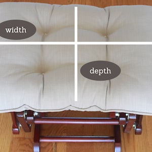 May include: Beige fabric ottoman with a tufted top and a wooden base. The ottoman is 20 inches wide and 16 inches deep.