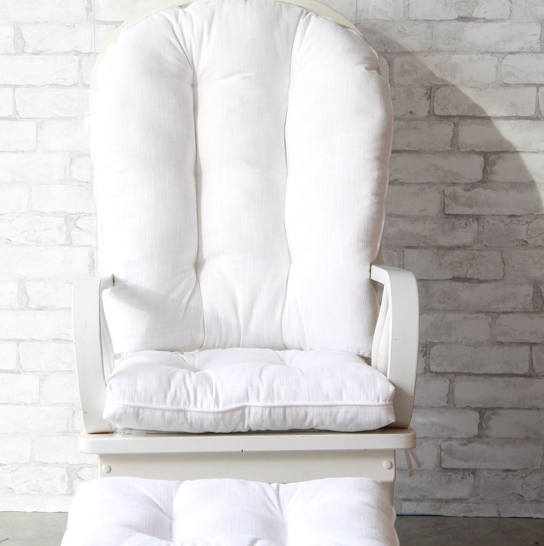 Puede incluir: Silla mecedora blanca con asiento acolchado y coj&iacute;n de respaldo. La silla tiene un marco de madera blanco y est&aacute; tapizada en tela blanca.