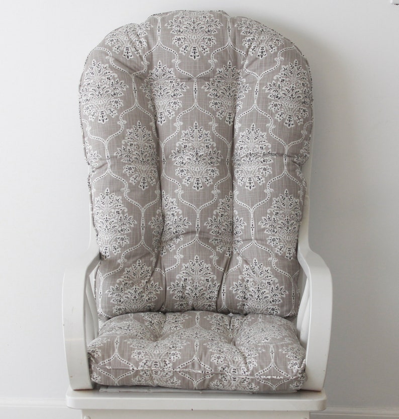 Puede incluir: Una silla mecedora blanca con un coj&iacute;n de patr&oacute;n gris y blanco. El coj&iacute;n tiene un dise&ntilde;o acolchado y est&aacute; relleno de relleno.