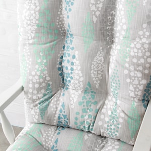Puede incluir: Un coj&iacute;n para silla mecedora gris y blanco con un patr&oacute;n de lunares azules y verdes.