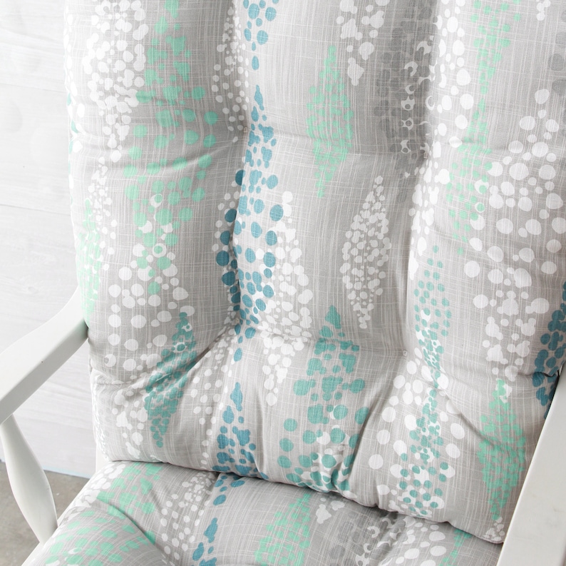 Puede incluir: Un coj&iacute;n para silla mecedora gris y blanco con un patr&oacute;n de lunares azules y verdes.