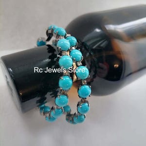 May include: A pair of turquoise bead bracelets with silver-colored settings. The bracelets are wrapped around a dark bottle. The text "Rc Jewels Store" is visible on the bottle.