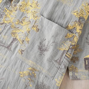 May include: Close-up of a gray garment with a pocket, featuring a repeating pattern of gold and brown trees and buildings. The fabric has a textured appearance, suggesting a linen or cotton blend.