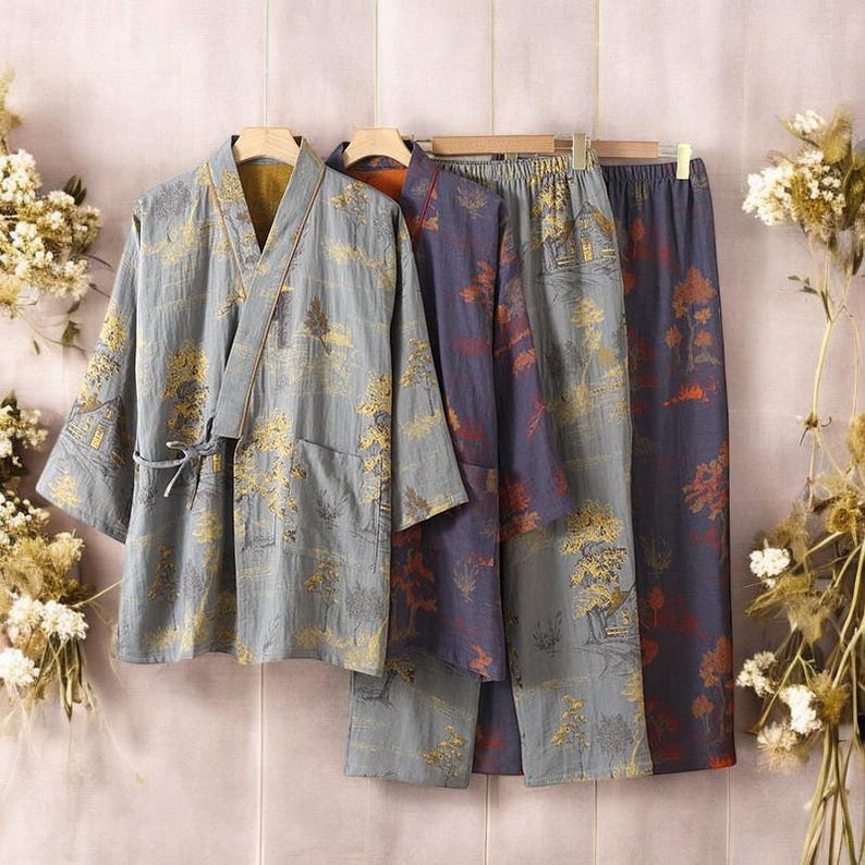 May include: Three-piece pajama set in a soft, muted color palette. The set includes a kimono-style top with a tie closure, and two pairs of pants. The fabric features a repeating pattern of trees and buildings in shades of gold, red, and blue.