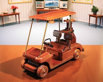 Puede incluir: Modelo detallado de carrito de golf de madera con acabado marrón. El carrito en miniatura cuenta con toldo, asientos, volante y almacenamiento de palos de golf. El carrito se exhibe sobre una mesa de madera en una habitación bien iluminada.