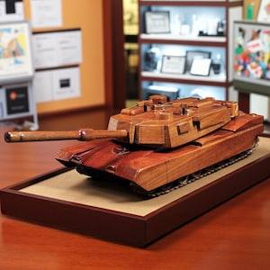 May include: A finely crafted wooden tank model, presented in a warm, reddish-brown colour. The model is displayed on a rectangular, dark brown base with a light tan surface. The tank's design includes a barrel, treads, and detailed body features.