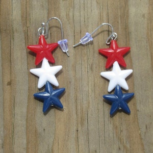 May include: A pair of dangle earrings with three stars each. The stars are red, white, and blue, reminiscent of the American flag.