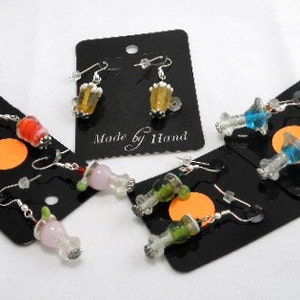 May include: Handmade glass earrings in various colors, including red, yellow, green, pink, and blue. Each pair is displayed on a black card with silver-tone ear wires. The text "Made by Hand" is visible on one of the cards.