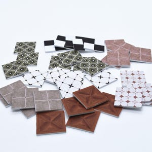 May include: A selection of square decorative tiles with diverse patterns and colours. Designs include floral, geometric, and chequered patterns in shades of brown, white, black, and grey. The tiles are arranged on a white surface.