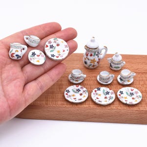 Può includere: Servizio da tè in miniatura in porcellana con disegni floreali. Il set comprende una teiera, una lattiera, una zuccheriera, tazze e piattini. I piatti e le tazze hanno bordi dorati. Il set è su una superficie di legno.