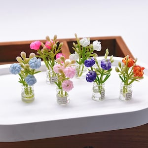Könnte beinhalten: Miniatur-Blumenarrangements in kleinen Glasvasen. Jede Vase enthält eine andersfarbige Blume, darunter blau, rosa, weiß, lila und orange. Die Vasen sind auf einem weißen Tablett angeordnet, mit dem Text "beautiful every day" auf jeder Vase.