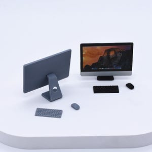 Può includere: Un set di computer in miniatura con un monitor grigio, tastiera e mouse. Il monitor mostra un'immagine del paesaggio. Il retro del monitor è visibile, insieme a una seconda tastiera e mouse.