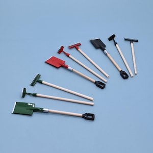 May include: A selection of miniature gardening tools, including shovels and rakes, with wooden handles and black or red heads. The tools are arranged on a light blue surface, highlighting their small size and detail.