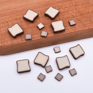 Puede incluir: Rebanadas de pan en miniatura con centros blancos y cortezas marrones dispersas sobre una tabla de cortar de madera y una superficie blanca. Las piezas de pan varían en tamaño, algunas cuadradas y otras rectangulares.