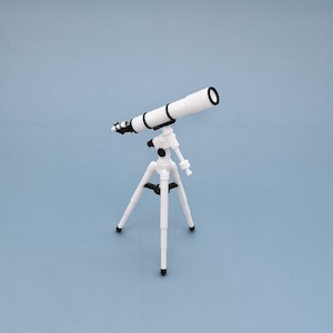 May include: A white toy telescope with black accents is mounted on a white tripod. The telescope is angled upwards, suggesting a focus on celestial observation. The background is a solid light blue.