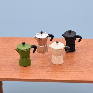 Pode incluir: Miniaturas de cafeteiras nas cores verde, prata, preto e creme. Cada uma tem uma alça e tampa pretas. Estão dispostas sobre uma superfície de madeira contra um fundo azul. Estas pequenas cafeteiras são provavelmente para uma casa de bonecas ou uma coleção em miniatura.