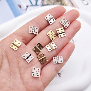 May include: A selection of small, square-shaped hinges in gold and silver. Each hinge has two leaves and a central barrel. These miniature metal hinges are suitable for small-scale craft projects, such as dollhouses or model making.