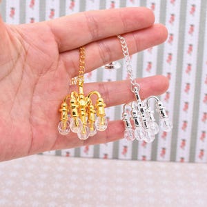 Puede incluir: Candelabros en miniatura, uno dorado y otro plateado, cada uno con detalles transparentes facetados en forma de bombilla. El candelabro dorado tiene una cadena dorada, y el plateado tiene una cadena plateada. Para casas de muñecas o proyectos.