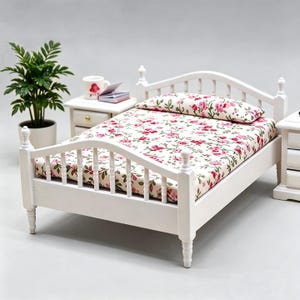 May include: A miniature white wooden bed with a floral patterned mattress and pillow. The bed frame has a headboard and footboard with rounded spindles. A small white bedside table with a drawer is next to the bed. A potted plant is in the background.