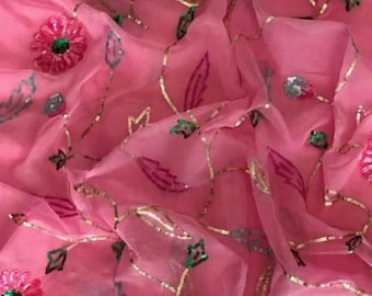 May include: Pink fabric with floral and leaf embroidery. The fabric has a sheer quality, with gold thread outlining the floral and leaf designs. The flowers are pink with green centers, and the leaves are pink and green.