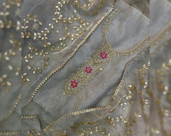 May include: A light grey embroidered tunic and matching scarf set. The tunic features gold and pink floral embroidery along the neckline and centre. The sheer scarf is adorned with gold leaf-like embellishments and a gold trim.