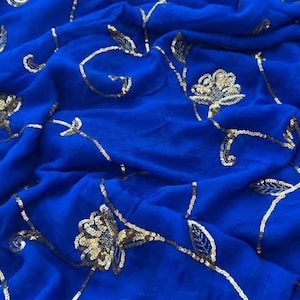 May include: A royal blue fabric with gold floral embroidery. The fabric is draped, showing the texture and design. The gold embroidery includes flowers and leaf patterns, creating an elegant look.