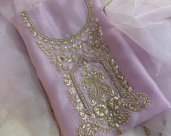 May include: A lilac salwar kameez set featuring detailed gold embroidery on the neckline and bodice. The set includes a matching dupatta with gold edging. The fabric is a sheer, flowing material.