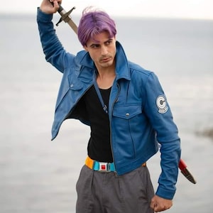 May include: A blue leather jacket with a 'C' patch, black shirt, gray pants, and a colorful belt. The person is holding a sword with a black handle and silver blade. The person has purple hair.
