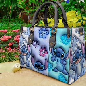 K&ouml;nnte beinhalten: Eine Tragetasche mit Stitch-Design aus Lilo & Stitch. Die Tasche hat einen hellblauen Hintergrund mit Stitch, Blumen und Bl&auml;ttermustern. Sie hat schwarze Griffe und goldfarbene Beschl&auml;ge. Ein farbenfrohes Accessoire.