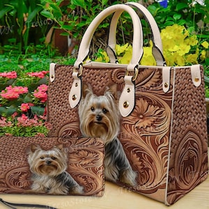 May include: A brown handbag and matching wallet set featuring a Yorkshire Terrier dog design. The bag has a woven texture with floral accents and cream-colored handles. The wallet has a wrist strap.