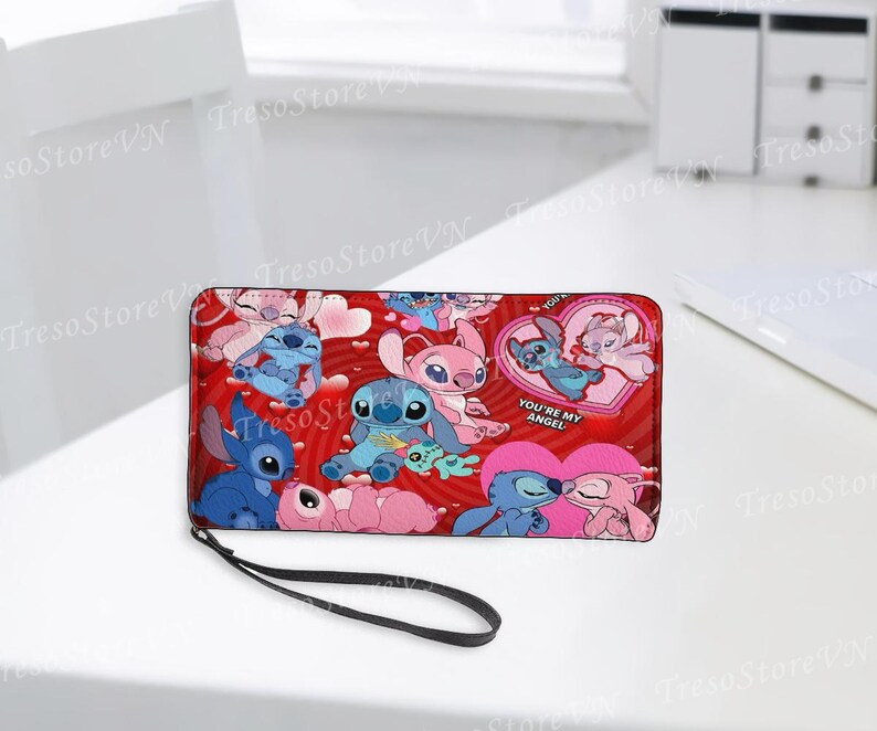Puede incluir: Cartera roja con los personajes de dibujos animados Stitch y Angel, corazones y el texto "YOU'RE MY ANGEL". La cartera tiene una correa de mu&ntilde;eca negra. El dise&ntilde;o presenta varias poses de los personajes.