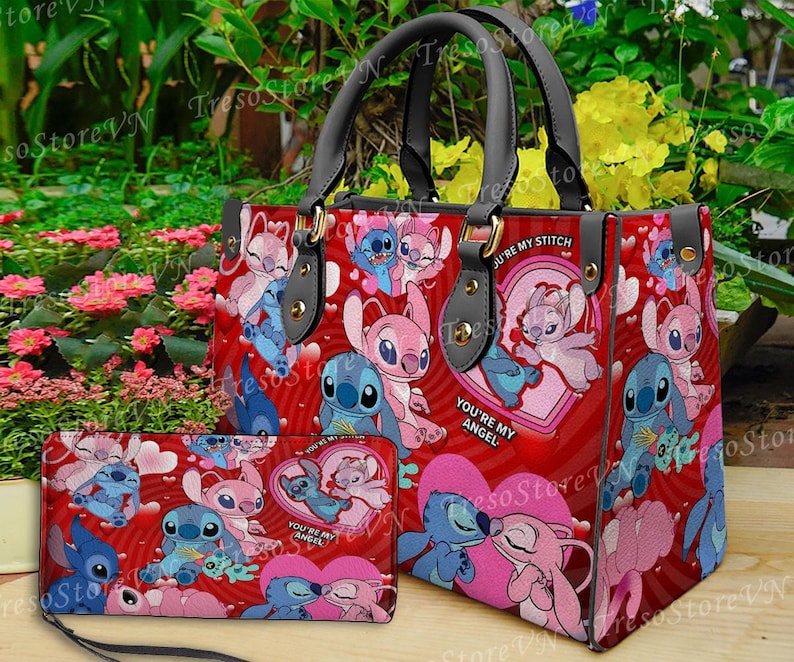 Puede incluir: Un bolso de mano rojo y una cartera a juego con un patr&oacute;n repetido de personajes de dibujos animados, corazones y las frases "You're My Angel" y "You're My Stitch". El bolso tiene asas negras y herrajes dorados.
