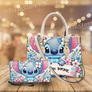 May include: A matching handbag and wallet set featuring a cartoon character design. The handbag has a cream-colored handle and shoulder strap, with a blue and pink floral pattern. The wallet has a wrist strap. The set is on a wooden surface.