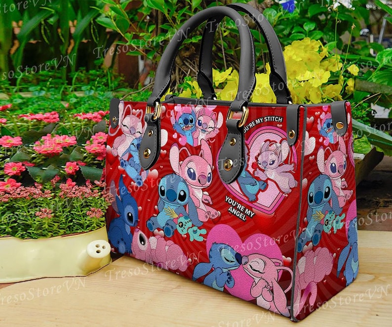 Puede incluir: Un bolso de mano rojo con un patr&oacute;n repetido de personajes de dibujos animados, corazones y las frases "You're my Stitch" y "You're my Angel". El bolso tiene asas y detalles en negro.