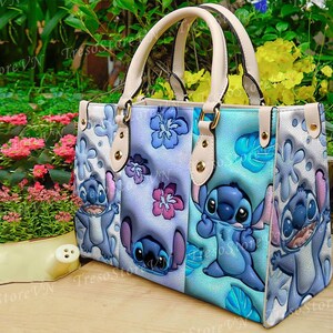 K&ouml;nnte beinhalten: Eine Tragetasche mit einem farbenfrohen Design mit der Figur Stitch aus Lilo & Stitch. Die Tasche hat ein hellblaues, lila und wei&szlig;es Farbschema mit Stitch-Illustrationen und floralen Akzenten. Sie hat cremefarbene Griffe und goldfarbene Hardware.