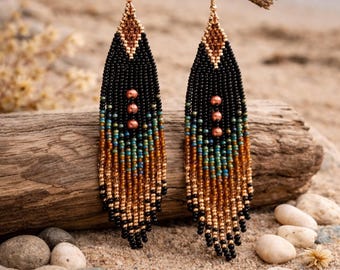 May include: A pair of beaded earrings with a feather design. The earrings feature black, brown, teal, and gold beads. The top portion is a diamond shape with a brown pattern. Three copper-colored beads are in the center of the earrings. The earrings hang from gold-colored hooks.