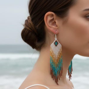 May include: Long, beaded earrings with a diamond-shaped top and a fringe of beads in white, gold, turquoise, and brown. The earrings hang from silver hooks, creating a striking contrast against the skin.