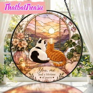 Könnte beinhalten: Ein runder Buntglas-Sonnenfänger mit einer schwarz-weißen Katze und einer orangefarbenen getigerten Katze, die gemeinsam auf einen Sonnenuntergang über dem Wasser blicken. Eine Blumenvase, eine Kerze und der Text You, me and a lifetime of purrs.