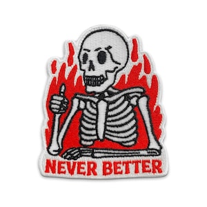 May include: Embroidered patch featuring a white skeleton giving a thumbs-up gesture, set against a red flame design. The phrase "NEVER BETTER" is displayed in red text at the bottom. The patch has a white border.