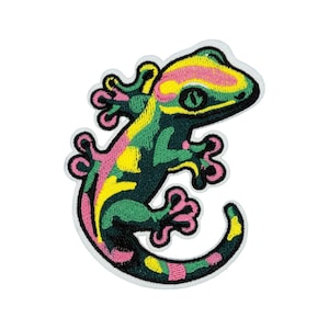 May include: Embroidered patch featuring a colorful gecko design. The gecko has a dark green body with pink, yellow, and green accents. The patch has a white border and is suitable for clothing or accessories.