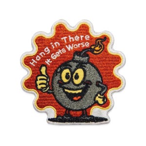May include: Embroidered patch featuring a cartoon bomb character with a smiling face and thumbs up. The patch is set against a red background with the text "Hang in There It Gets Worse" in white lettering. The patch has a white scalloped border.