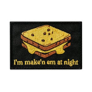 May include: Embroidered patch featuring a grilled cheese sandwich with melted cheese. The patch is black with yellow and brown details. Text at the bottom reads "I'm make'n em at night".