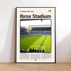 May include: A framed poster featuring Ibrox Stadium in Glasgow, Scotland. The image shows the green field and stands of the stadium, with the text "Ibrox Stadium" at the top. The poster is in a black frame and is displayed against a white wall.