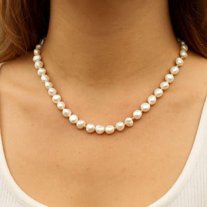 May include: A delicate pearl necklace featuring lustrous, off-white pearls strung together with gold-colored accents. The necklace is displayed against a neutral background, highlighting the classic elegance of the jewelry.