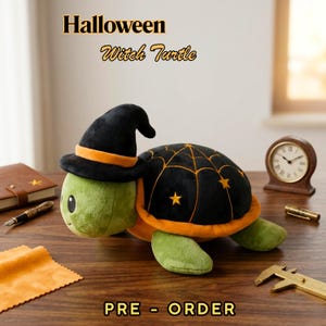 May include: A plush green turtle wearing a black witch hat with an orange band and a black shell decorated with an orange spiderweb and stars. The text "Halloween Witch Turtle" and "PRE - ORDER" are visible.