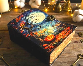 May include: A decorative book with a Halloween-themed cover featuring a full moon, a tree, and a jack-o'-lantern. The book has a dark cover with a metal clasp and aged, yellowed pages. The scene is set in a forest with autumn colors.