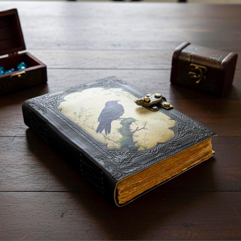 Pu&ograve; includere: Un diario rilegato in pelle nera con un design in rilievo e una chiusura in metallo. La copertina presenta un'illustrazione decorativa di un uccello viola appollaiato su un ramo. Le pagine invecchiate hanno una tonalit&agrave; dorata, suggerendo un'estetica vintage.