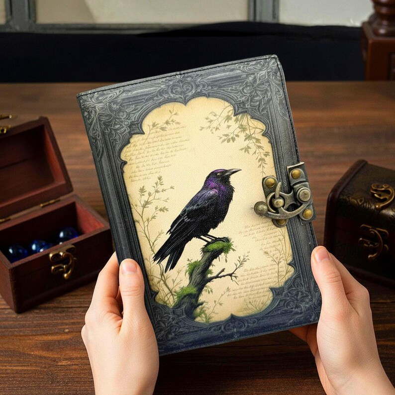 Pu&ograve; includere: Un diario grigio scuro con un'illustrazione di un corvo. La copertina presenta un corvo nero con riflessi viola appollaiato su un ramo muschioso, su uno sfondo simile a pergamena. Il diario ha una cornice ornata e una chiusura in metallo.